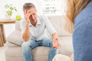 Man puts his forehead to his hand as he discusses difficult topics with his therapist in a relapse prevention treatment program